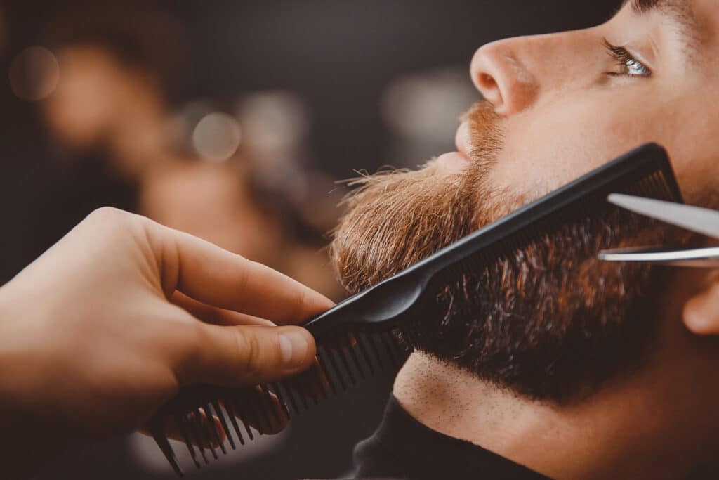Barbier taillant une barbe brune avec un peigne et des ciseaux de précision.