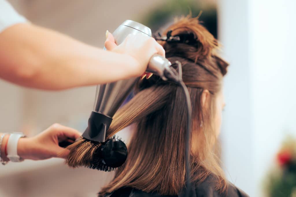 Coiffeuse effectuant un brushing professionnel avec brosse ronde.