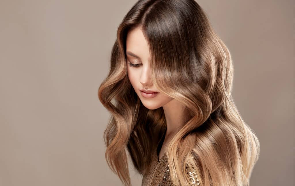 Cheveux longs ondulés avec balayage miel et châtain brillant sur fond neutre.